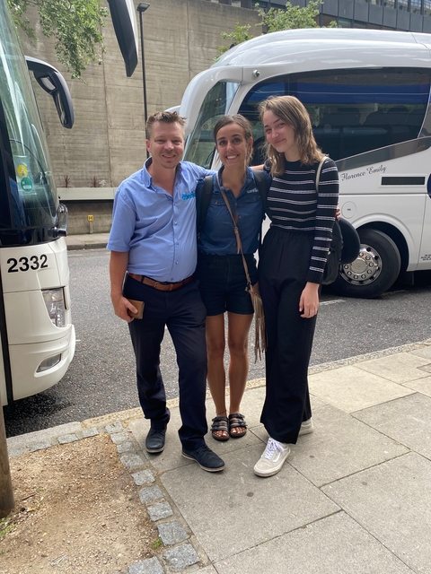 Three people smiling and posing for a photo on a street.