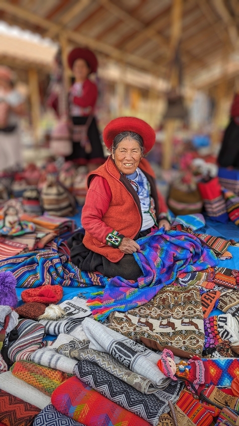 An elderly woman surrounded by textiles, smiling at the camera.