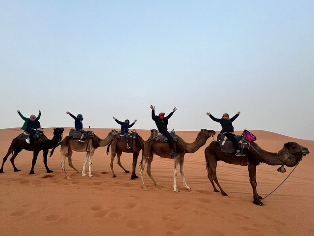 Camel ride with people raising their hands in the desert.