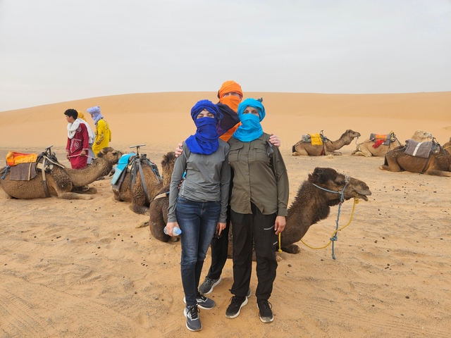       Group with camels in a desert, wearing traditional scarves.
  