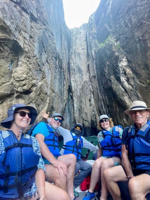       Group of people wearing life vests in front of a rocky cliff face.
  