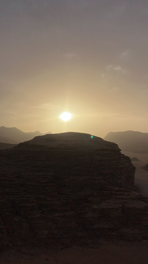 A sunset over a desert landscape with a silhouetted mountain.