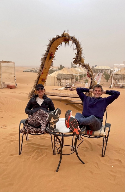 Two people relaxing in a desert camp with tents in the background.