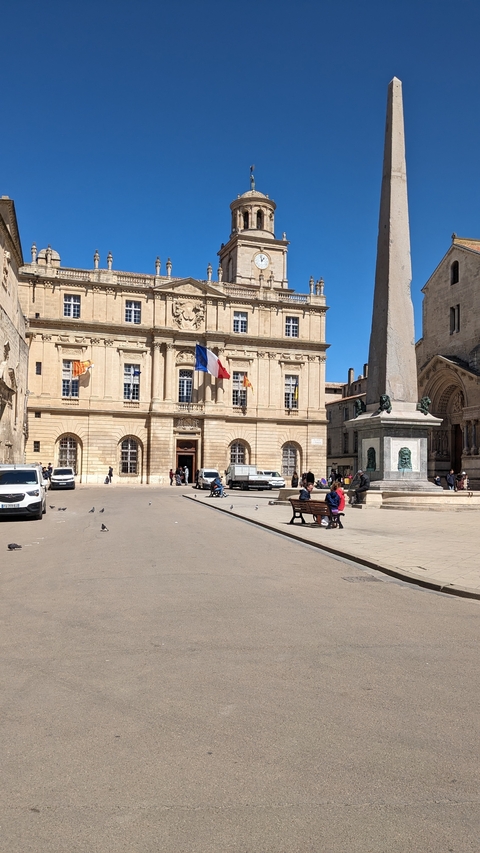 A public square with a historic building and an obelisk under a clear blue sky.