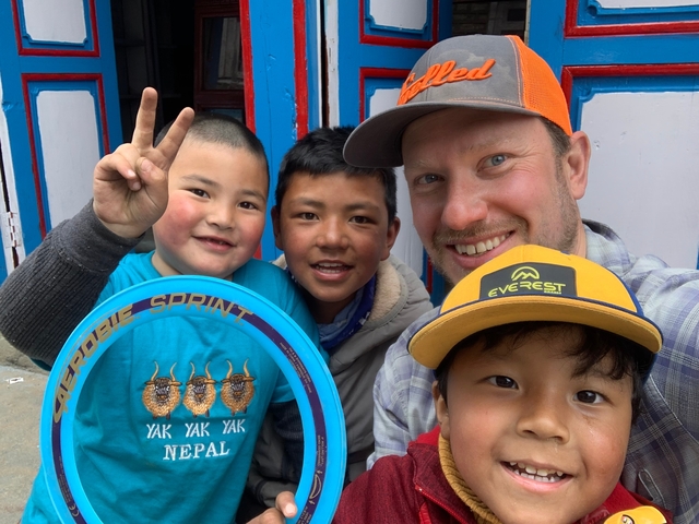       A group of smiling children with a man posing for a selfie.
  