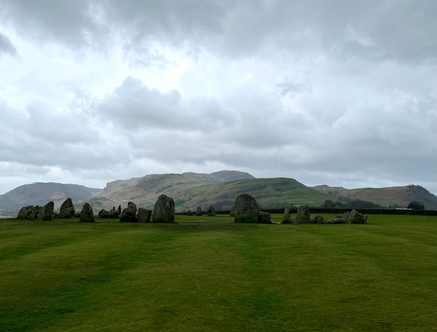       Stone circle in a grassy field surrounded by hills.
  