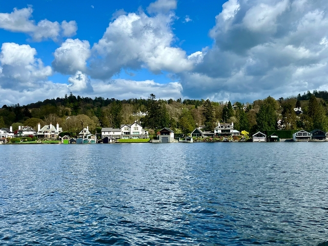 Lakeside houses with lush greenery and a cloudy sky.