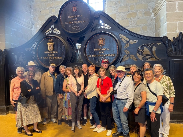 A group posed in front of large wooden wine casks with royal insignia.