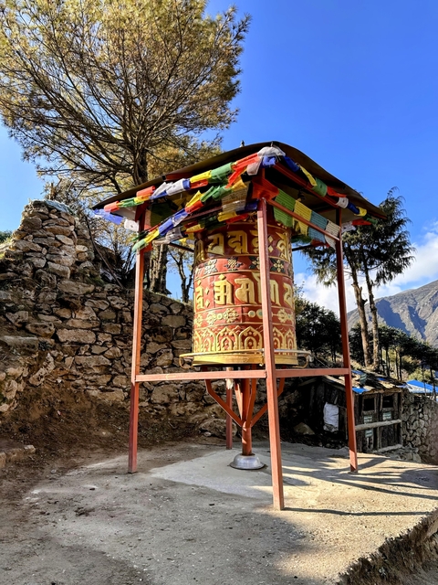 A colorful prayer wheel in a rural mountainous area with trees.