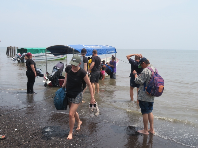 People wading near boats on a beach, preparing to depart.