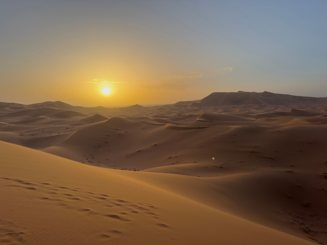       Desert landscape with sand dunes under a bright sunset.
  