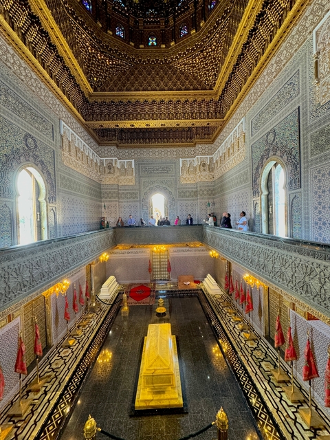       Interior of a palace with intricate tile work and people observing.
  