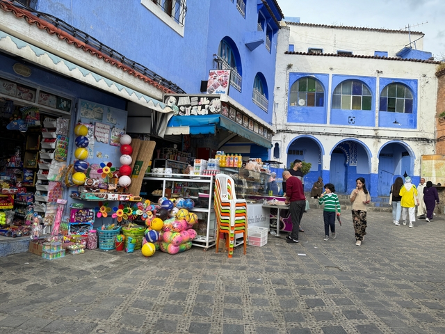       Street market scene with colorful buildings and people shopping.
  