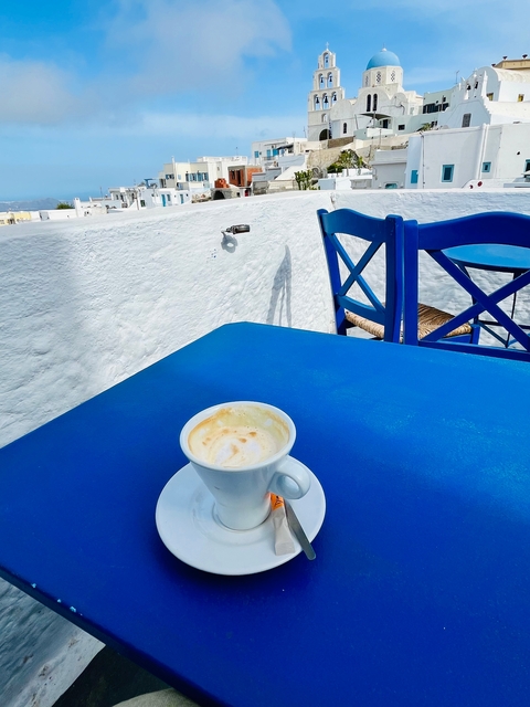 A cup of coffee on a blue table with matching blue chairs outside a white building.
