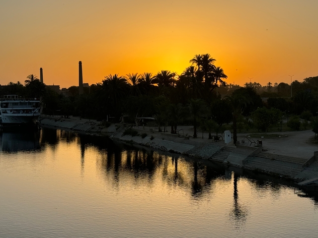 Sunset over a river lined with palm trees and boats.