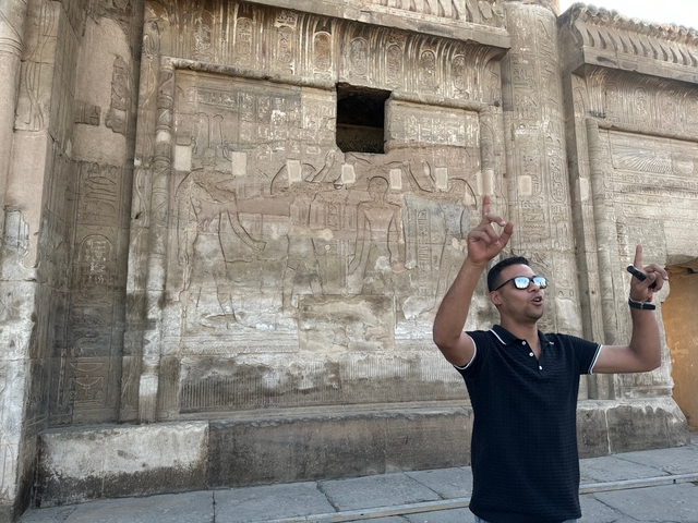 A guide speaking in front of ancient wall carvings.