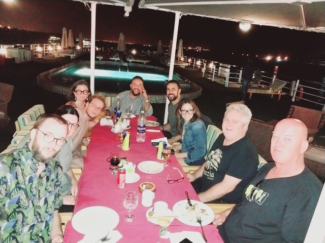       Group dining by a pool at night on a boat.
  