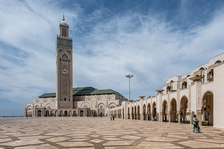       Large mosque with a tall minaret in an open courtyard with blue sky.
  