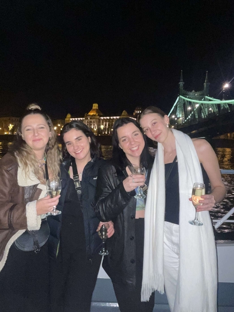 Group of women holding drinks, with lit bridge in the background.