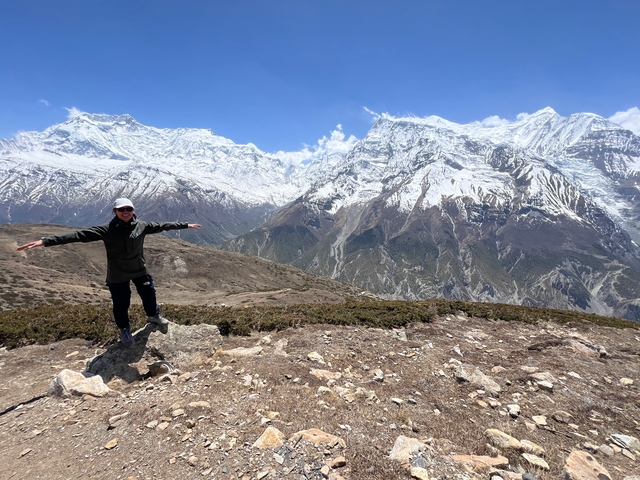 Person with arms outstretched standing against a mountainous backdrop.