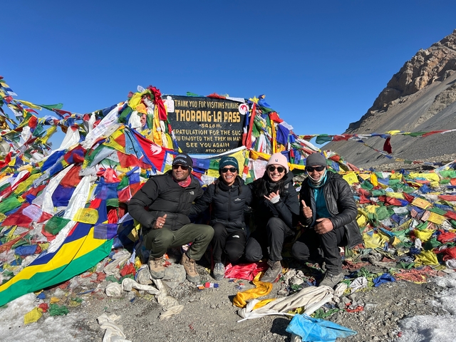 Group of trekkers posing at Thorong La pass, surrounded by flags.