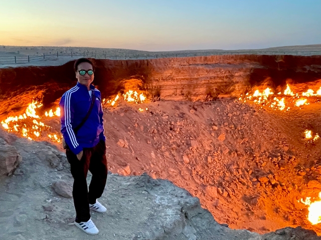 Person standing near a fiery crater in a desert landscape.