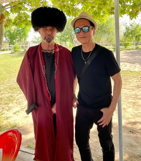       Two people standing with a traditional garment in a grassy area.
  