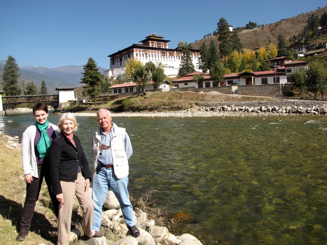 Three people by a river with a traditional fortress in the background.