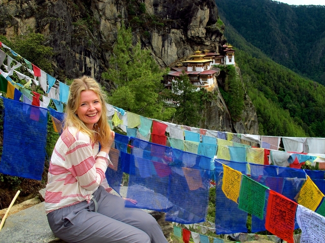 Woman smiling with prayer flags and mountain monastery.