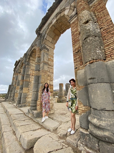 Two people standing among ancient ruins with arches.