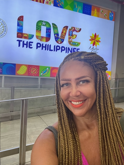       Smiling person with braided hair in front of a colorful 'Philippines' sign.
  