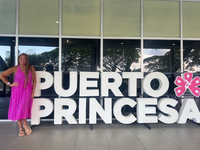       Person in a pink dress next to large 'Puerto Princesa' letters.
  