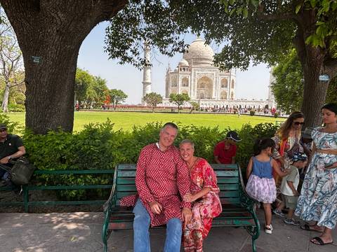       A couple sitting on a bench with the Taj Mahal in the background.
  