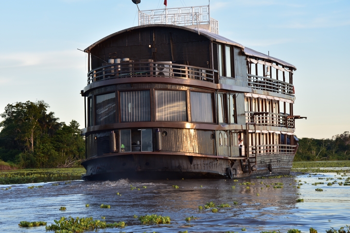 Large riverboat on the water with greenery surrounding.