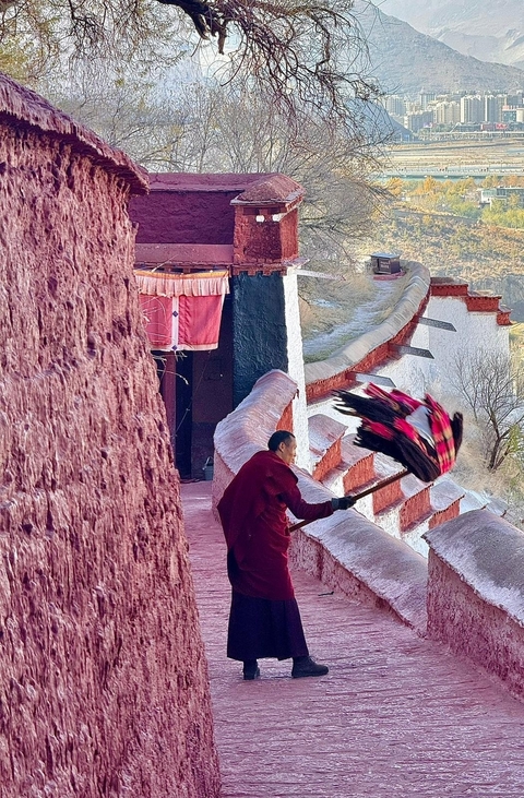 Man with a large red and black broom in a traditional setting.