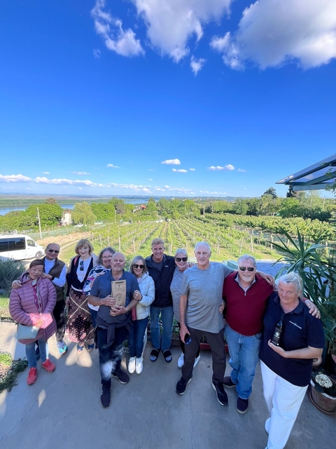 Group posing in front of a vineyard with blue skies.