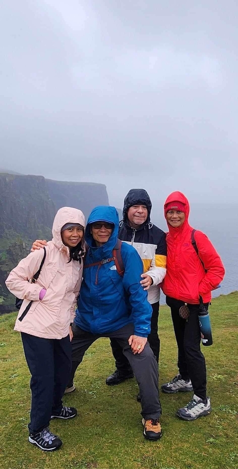Four people in raincoats posing at a cliffside.
