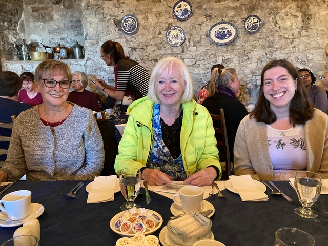 Three women at a dining table indoors with stone walls.