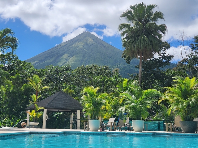       Arenal Volcano surrounded by lush greenery under a clear blue sky.
  
