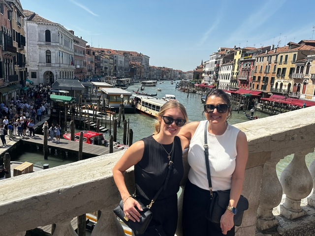 Two women posing on a bridge over a crowded canal with buildings.