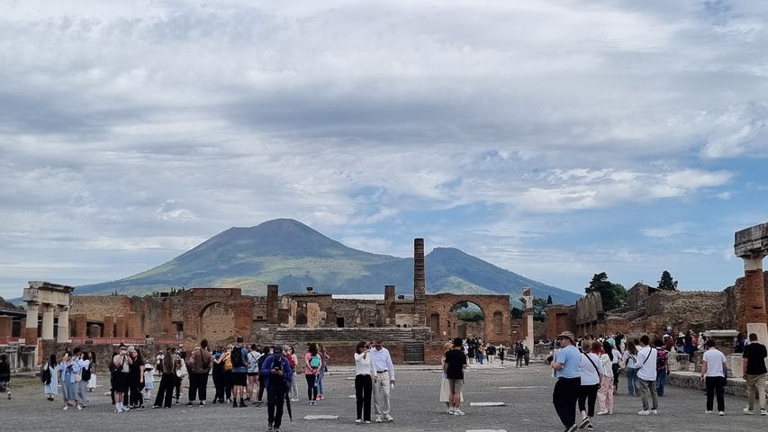 Ancient ruins with tourists and mountain backdrop.