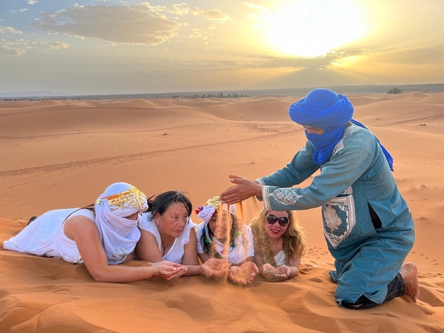       People in the desert pouring sand into each other's hands.
  