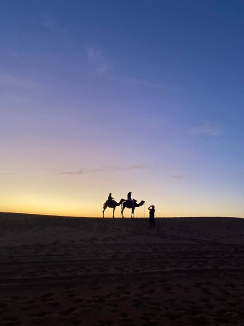       Silhouettes of people on camels at sunset.
  