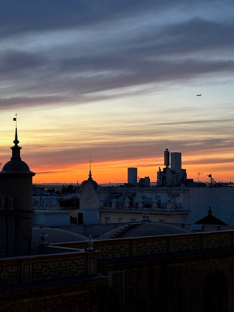       Dramatic sunset over city skyline with a silhouette of a tower.
  