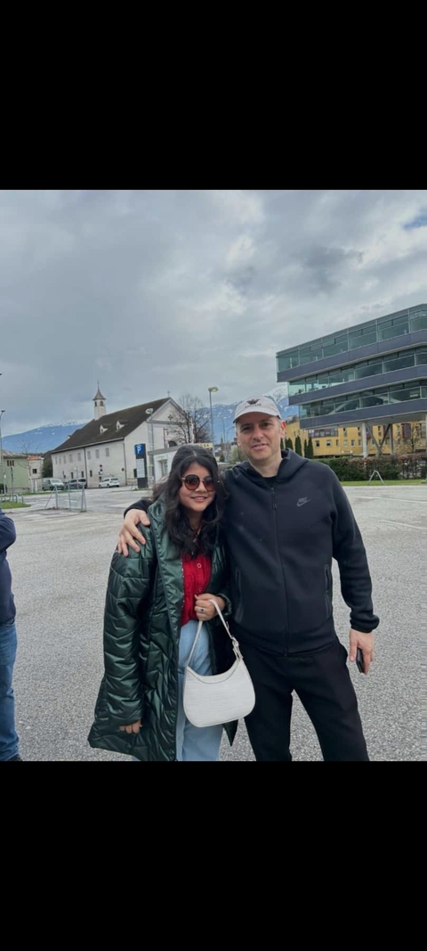       Two people posing outside modern buildings with mountains in the background.
  