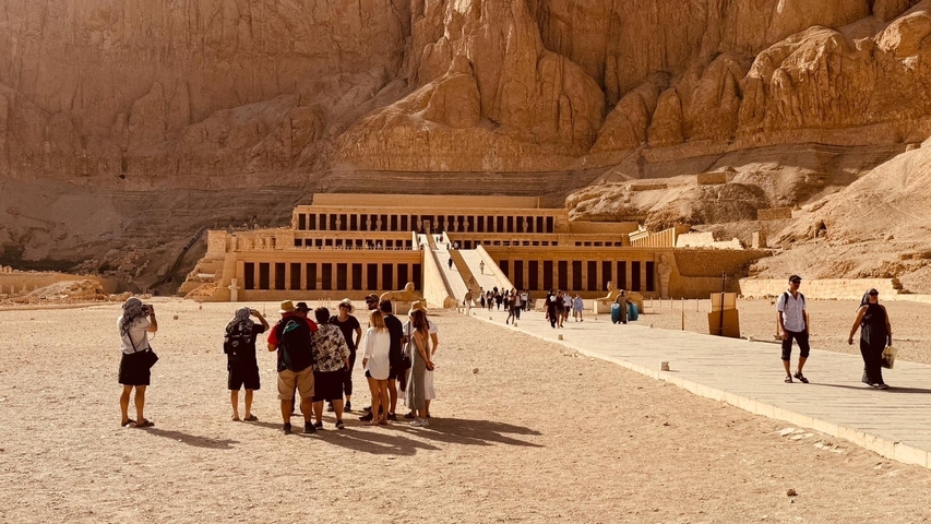      Temple in desert landscape with tourists gathered in front.
  