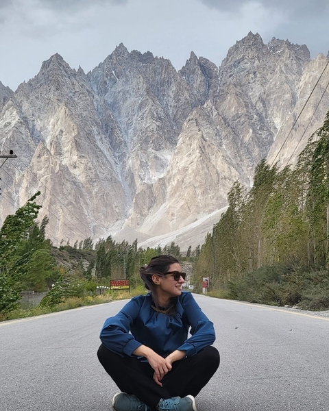 Person standing on a road with a dramatic mountain backdrop.
