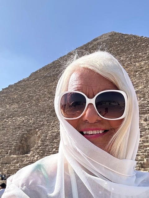       Close-up of sunglasses-wearing person with a pyramid structure in the background.
  