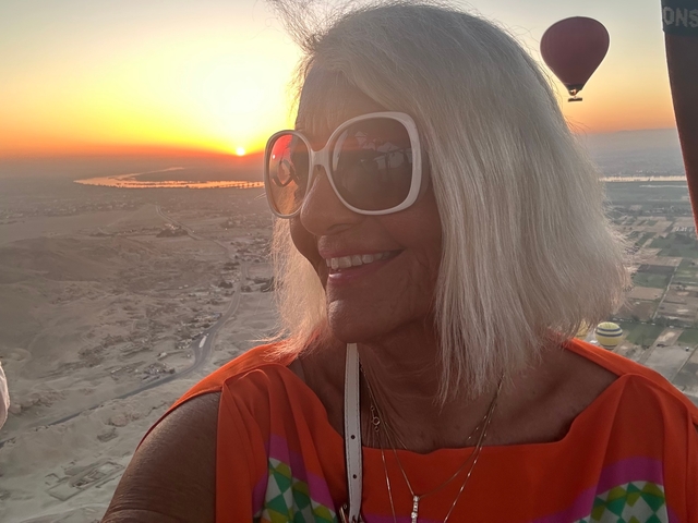      Woman enjoying a hot air balloon ride at sunset with expansive landscape views.
  