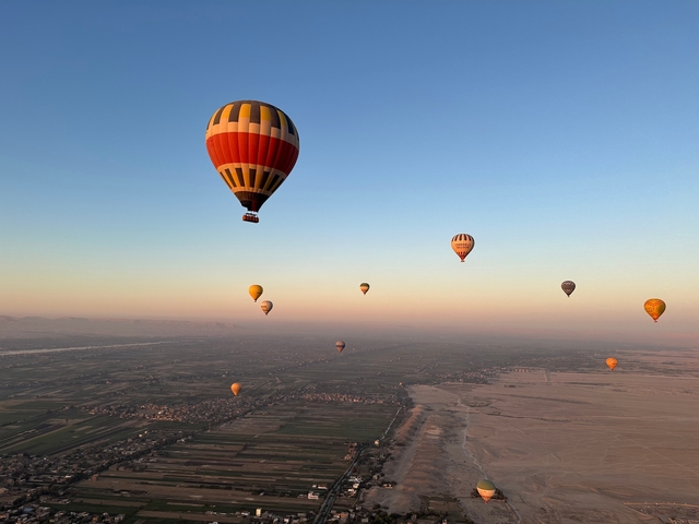       Hot air balloons in flight over landscapes at sunrise.
  